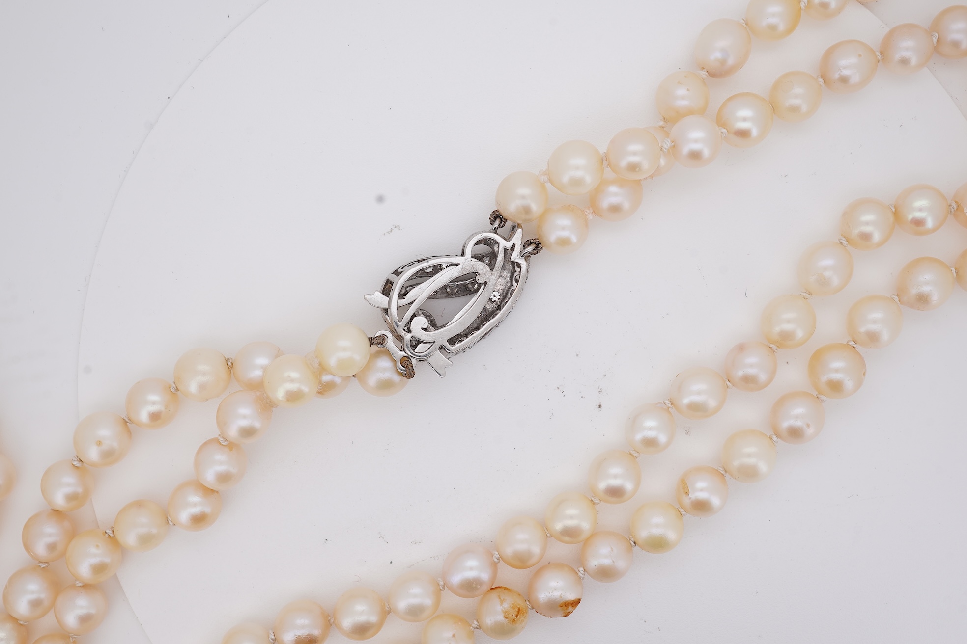 A twin strand cultured pearl necklace with a diamond cluster set white metal scroll shaped clasp, 60cm.